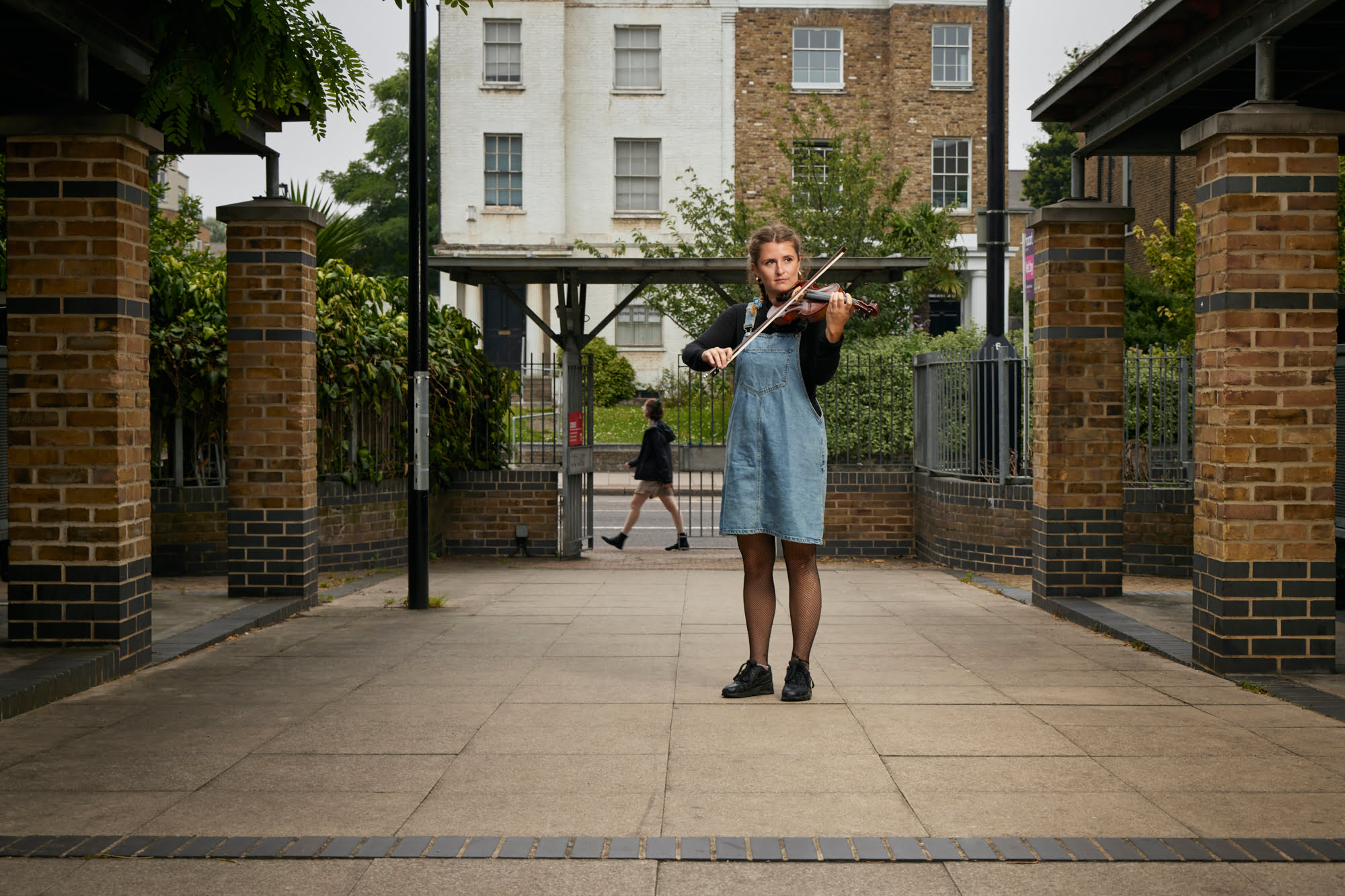 Ana Vandepeer, Angell Town Estate, looking onto Brixton Road. Principal violinist of Brixton Chamber Orchestra, pictured here at Leys Court, North Brixton, looking on to Brixton Road, ahead of a Summer Estates performance. The development was built in close consultation with residents, to replace the formidable and fortress-like 1970s Angell Town concrete block estate which taxi drivers often refused to enter. Open, light and close to the road while centered around communal spaces, Leys offers a very different living experience tailored by and for residents.